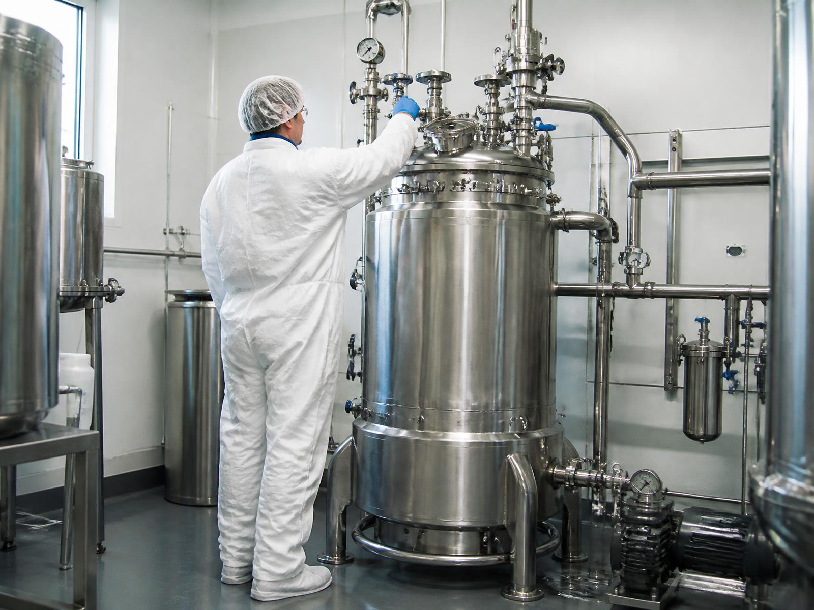 Stainless steel closed loop extraction vessel being operated by a gowned technician in the manufacturing suite.